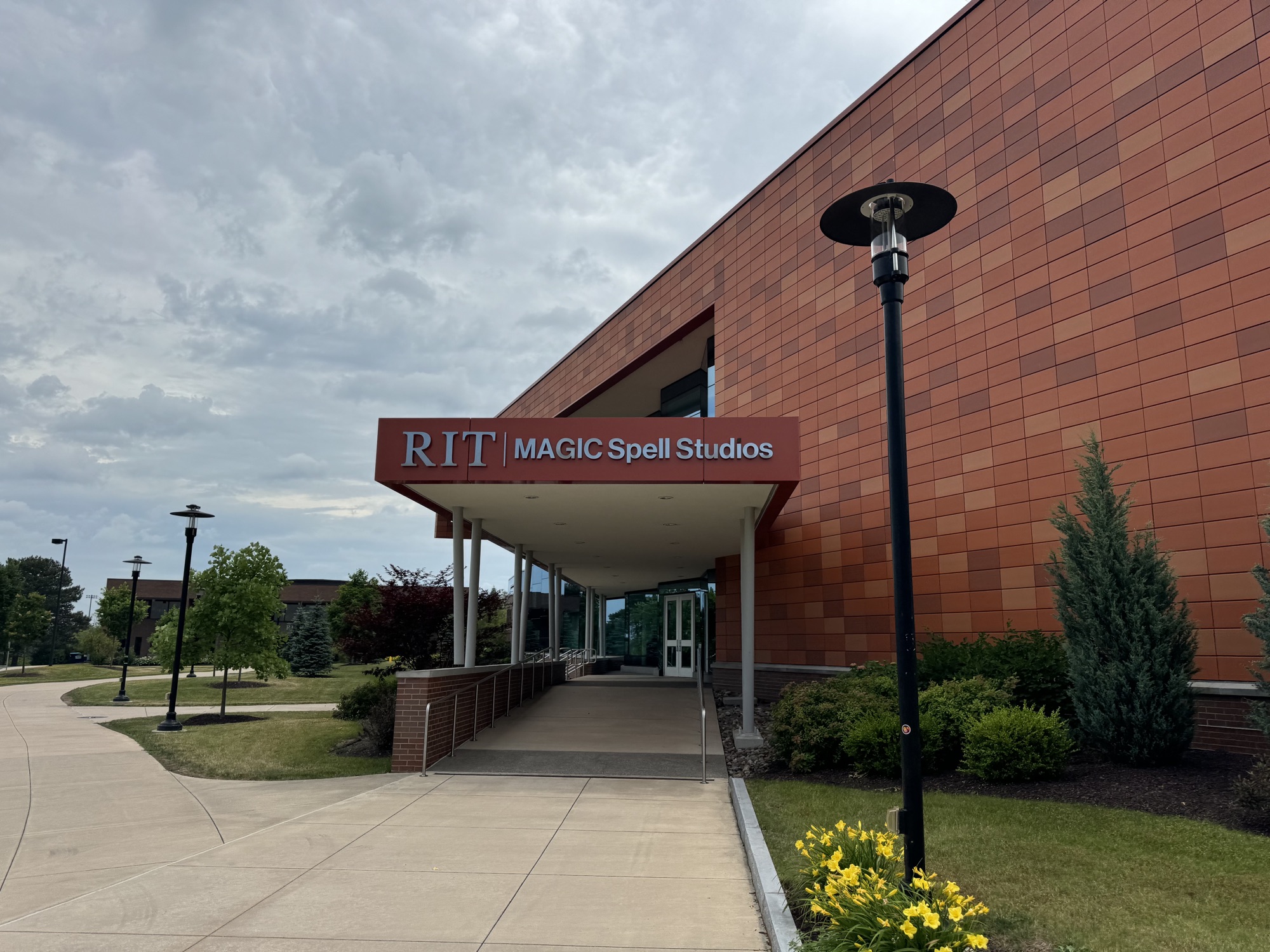 The entrance to RIT MAGIC Spell Studios, a long orange-tiled building under a cloudy sky